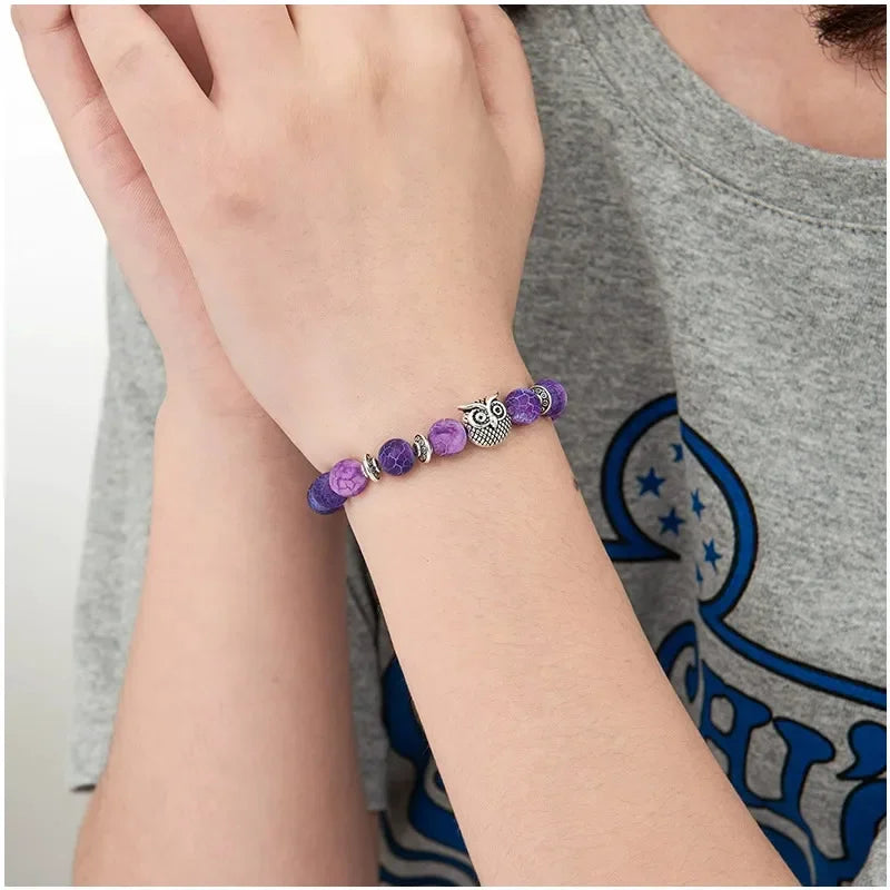 Person wearing purple beaded bracelet with owl charm and silver accents on wrist