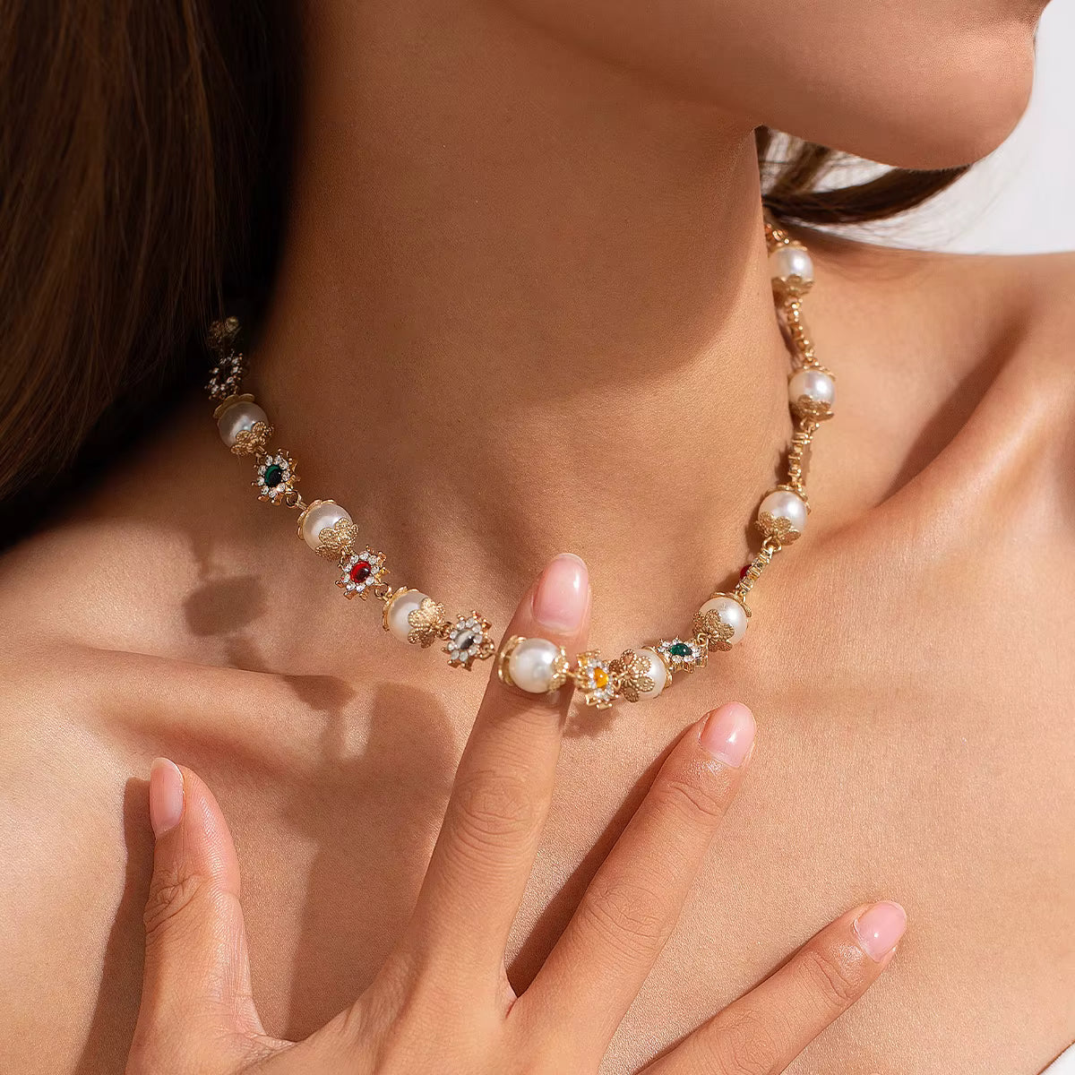 Close-up of woman wearing gold necklace with pearls and multicolored gemstone accents