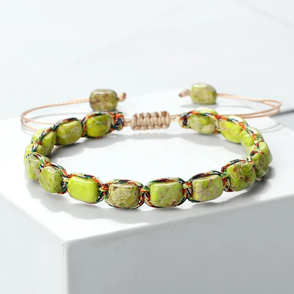 Green natural stone beaded bracelet with multicolor braided cord on white pedestal