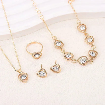 Gold jewelry set with heart-shaped clear crystals including necklace, ring, earrings, and bracelet on white surface