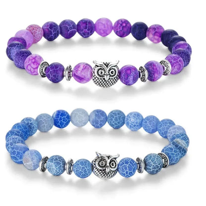 Purple and blue beaded bracelets with silver owl charm and decorative spacers on white background
