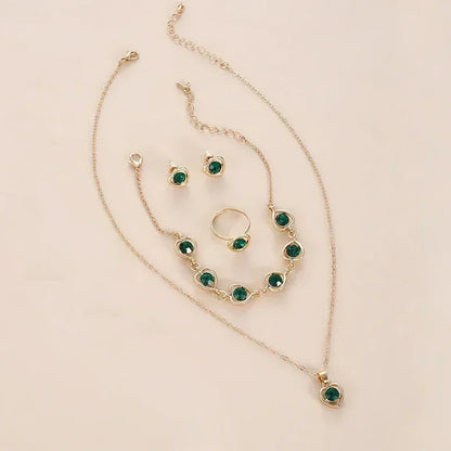 gold jewelry set with green gemstones including necklace, bracelet, ring, and earrings on beige background