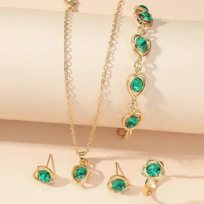gold jewelry set with green heart-shaped gemstones including necklace, bracelet, earrings, and ring on beige background