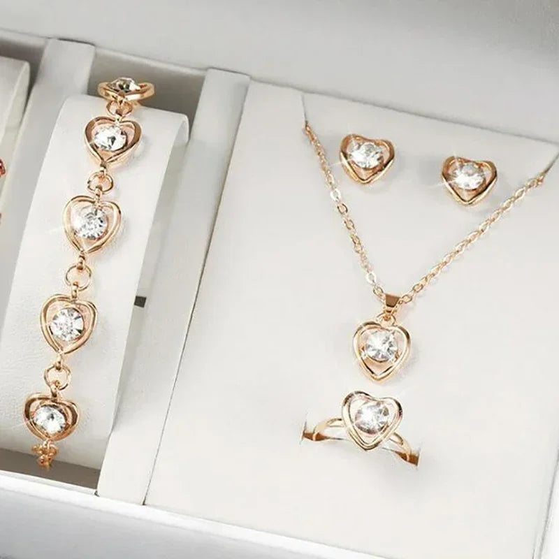 Gold heart-shaped jewelry set with clear gemstones including bracelet, necklace, earrings, and ring in white display box